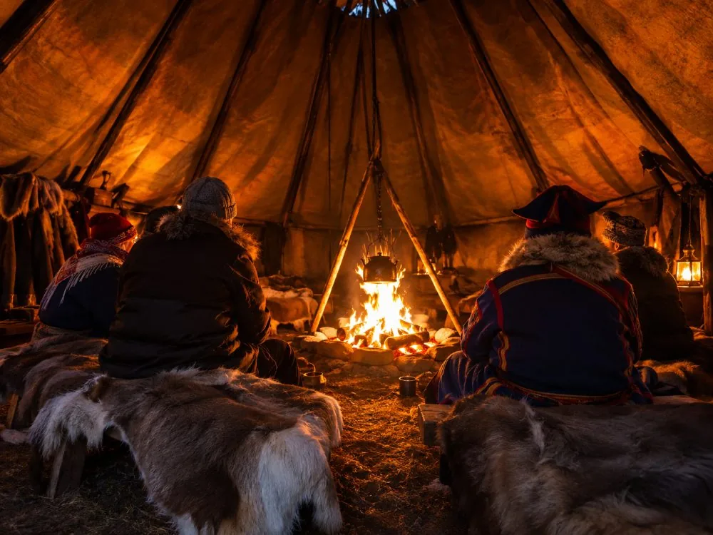 Fire burning inside a Sámi lávvu with guests sitting around it